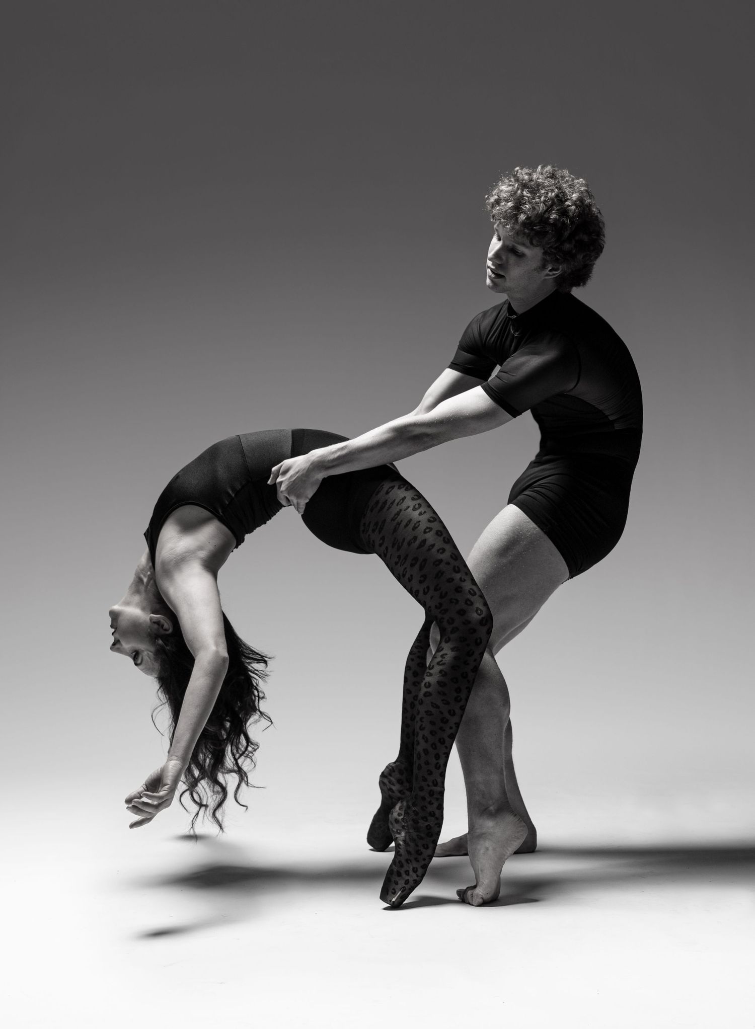 Black and white photo of a female dancer performing a contemporary dance pose on the floor, photographer Alec Watson