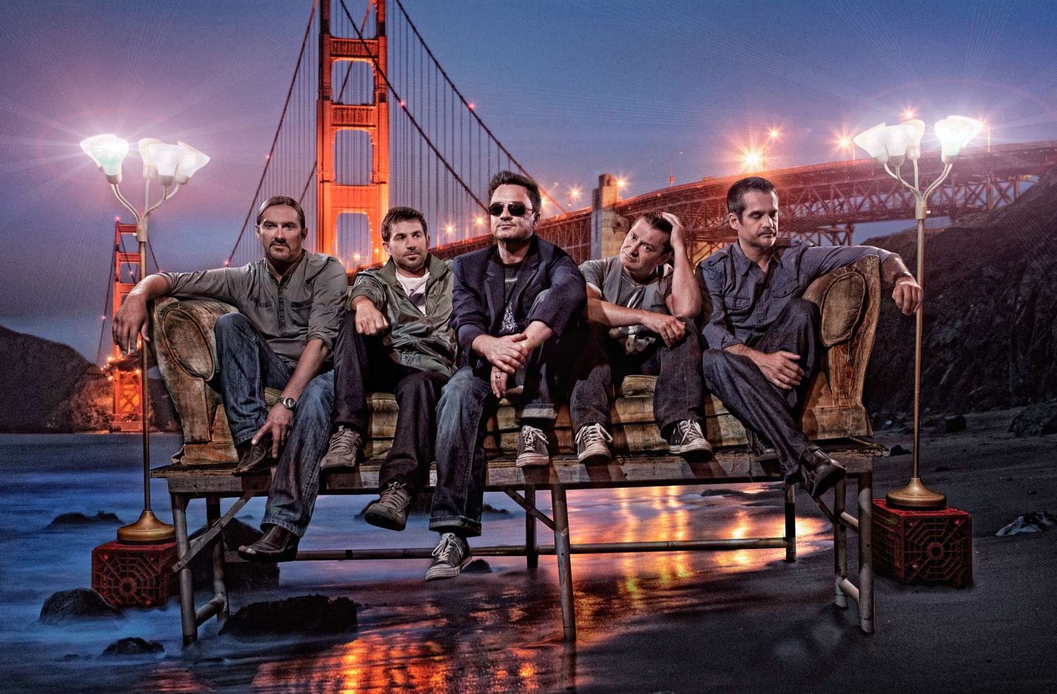 Composite image of a band performing on a stage with instruments and vintage lamps against a backdrop of a bridge at sunset photographer Ale