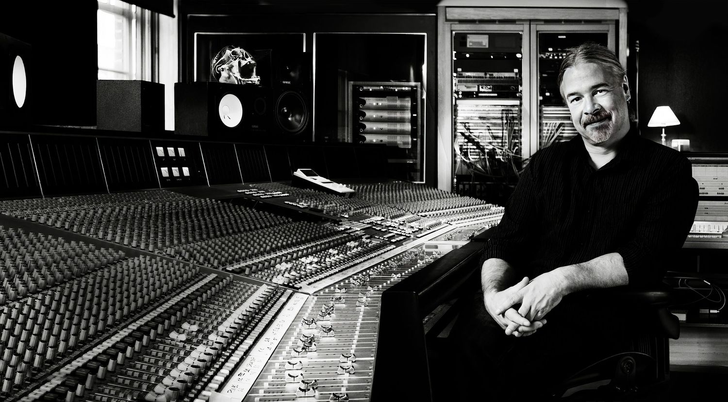 Black and white portrait of a man sitting in a recording studio surrounded by audio equipment, photographer Alec Watson