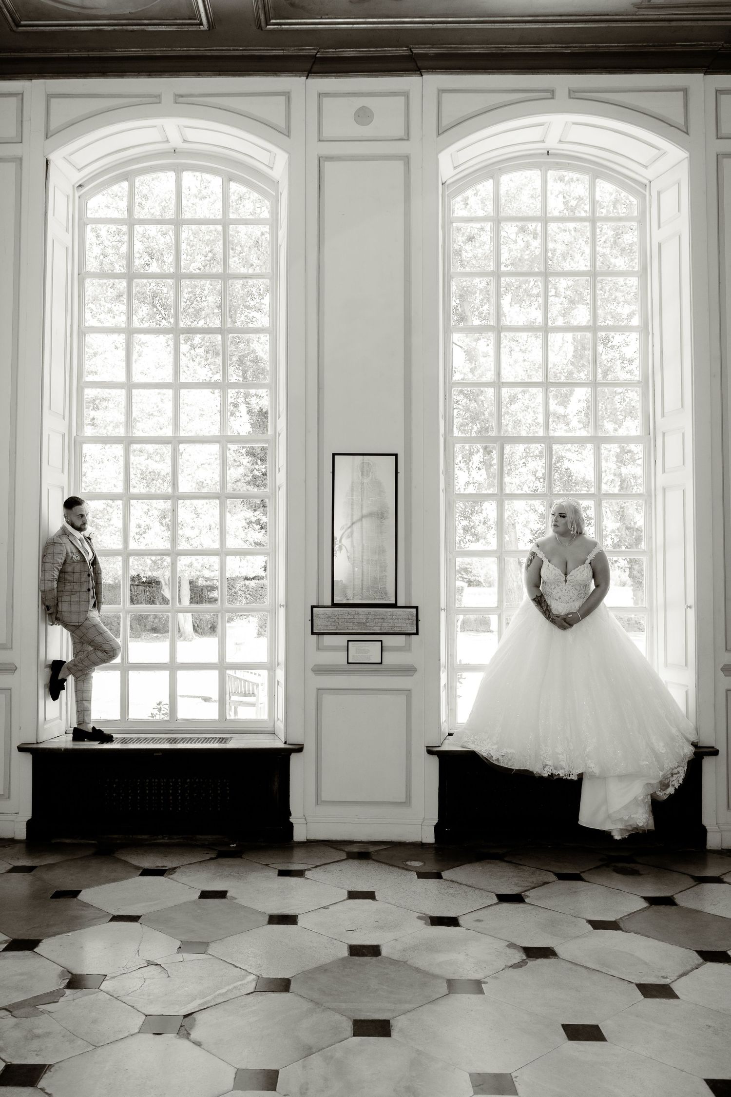 A creative black and white wedding photo with two people standing in grand windowed alcoves.