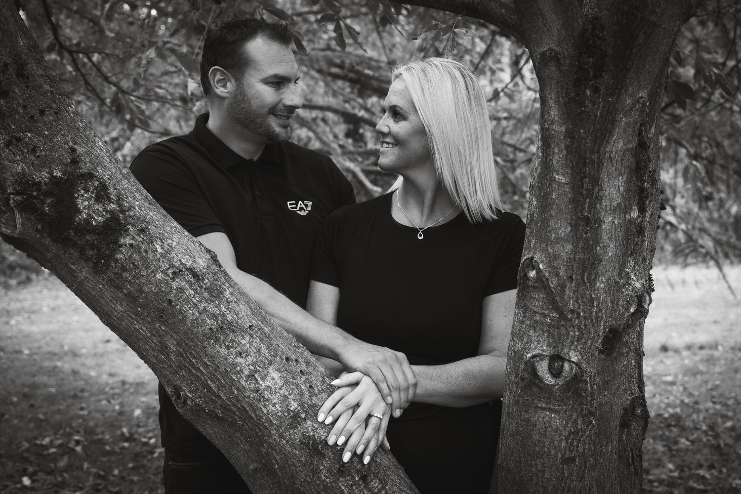 Black and white romantic engagement photos showing couple embracing near trees.