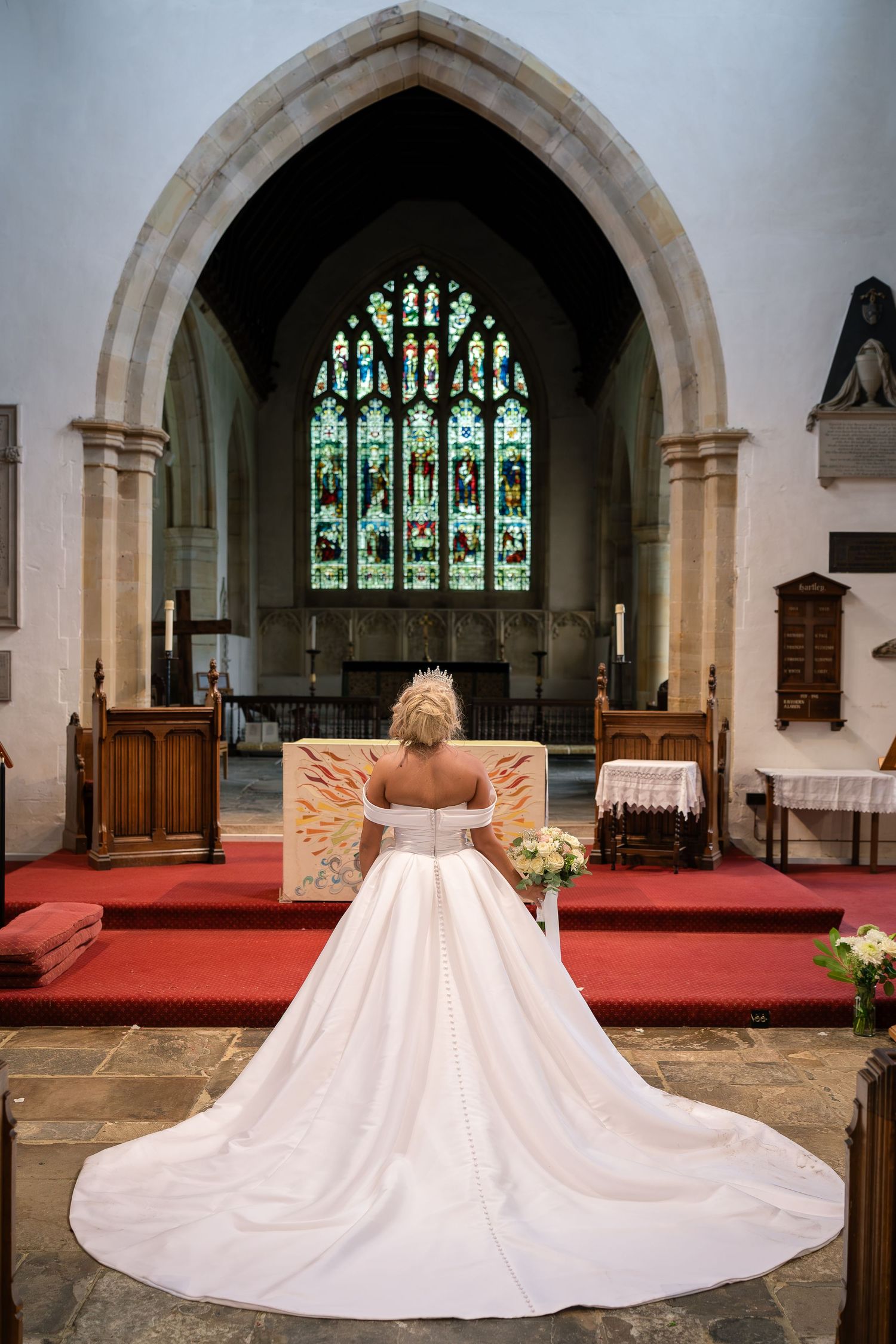 A wedding dress train spreads beautifully across red carpet in a historic church.
