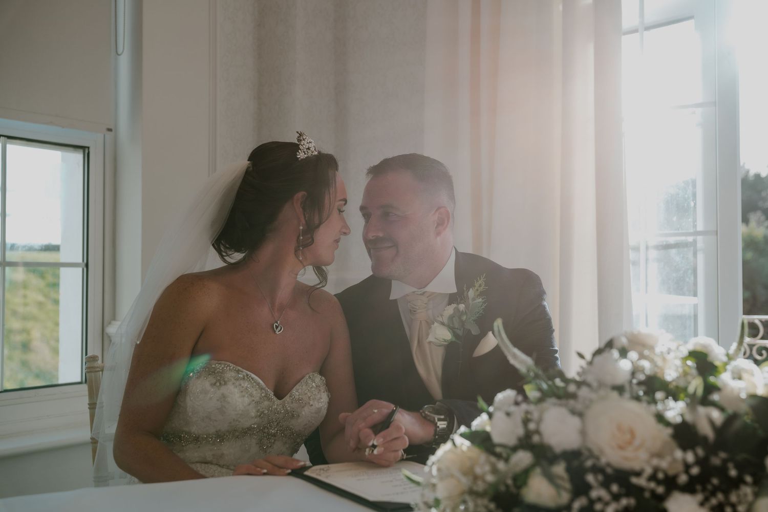 Sunlit indoor scene with white floral arrangements near bright windows.