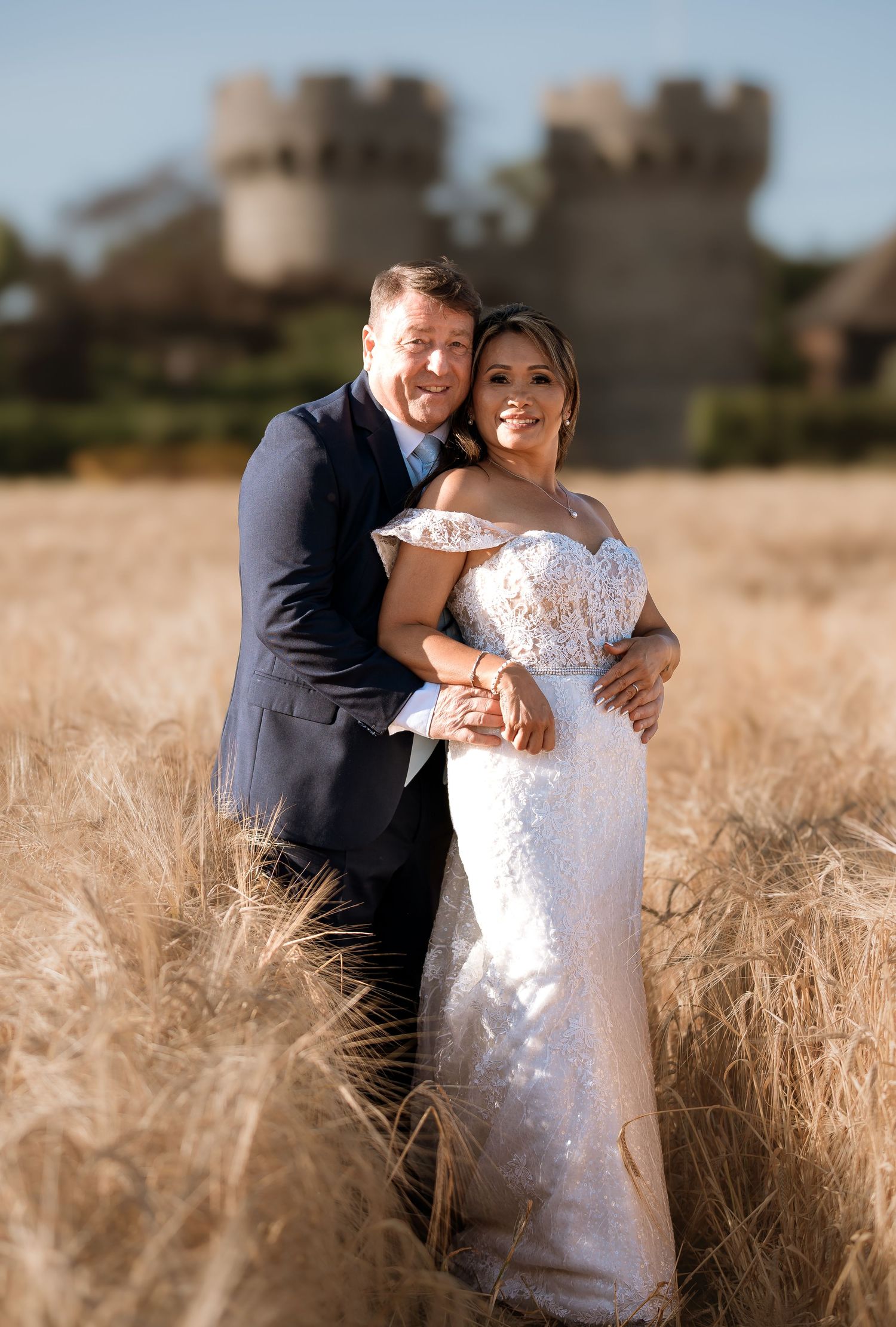 Couple embraces in golden wheat field on their wedding day.