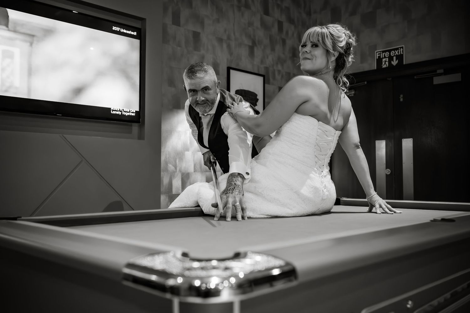 Black and white image of a wedding celebration around a pool table in casual setting.