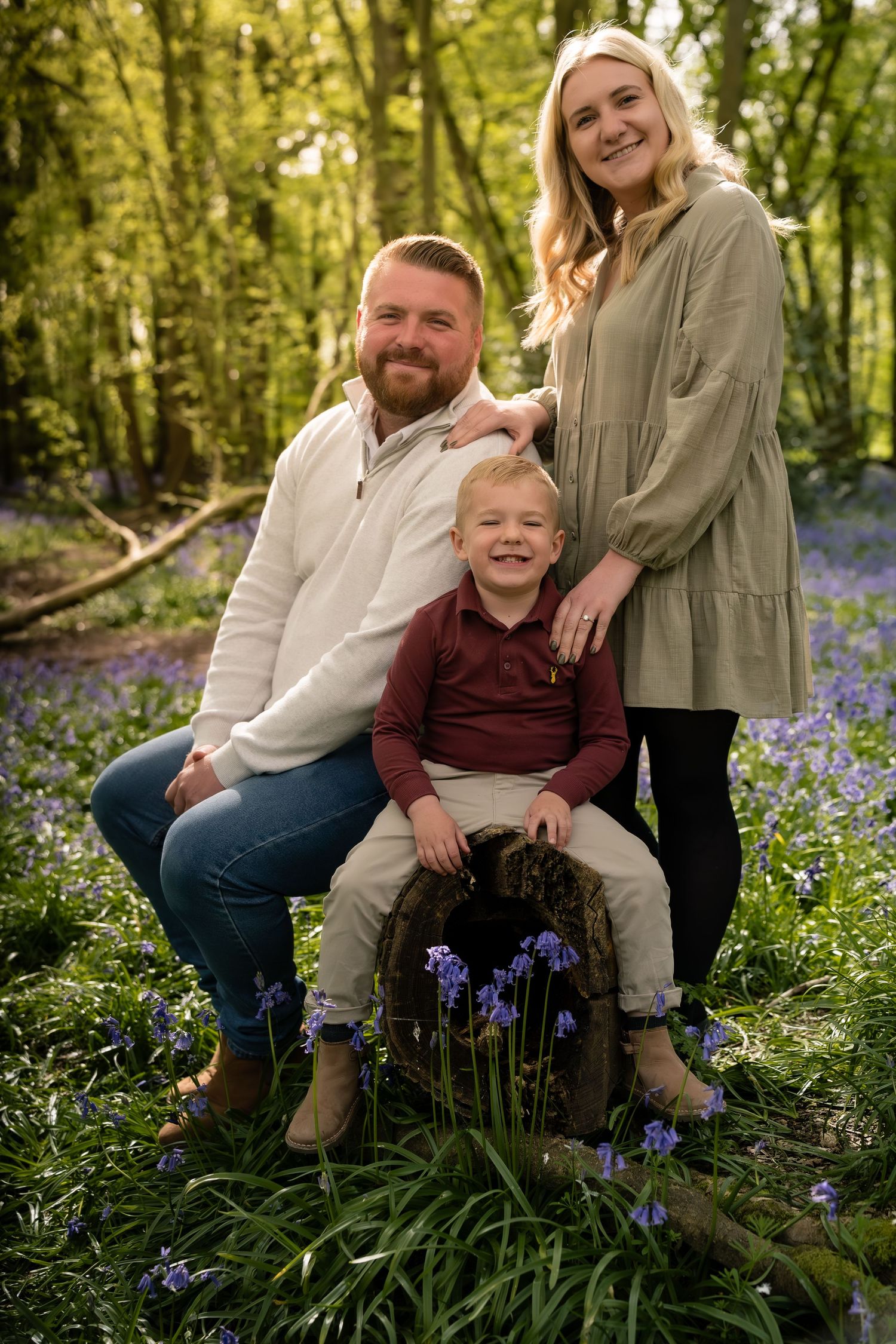 Family portrait session among blooming spring flowers in a sunlit forest.
