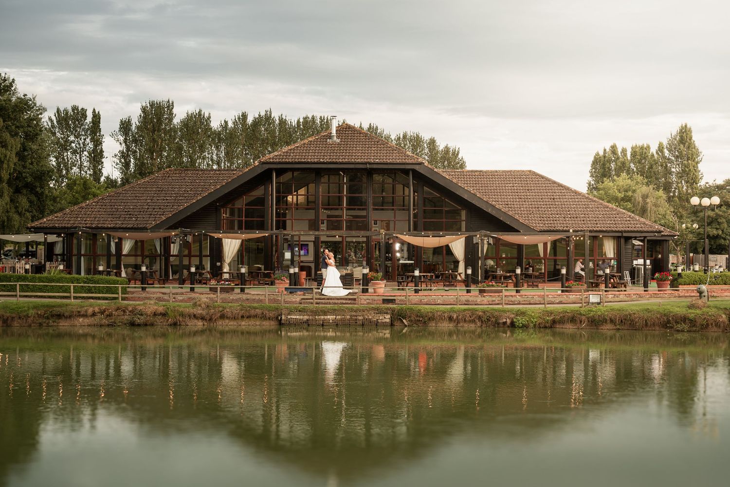 Rustic wooden wedding venue with reflective pond and trees in background during golden hour.