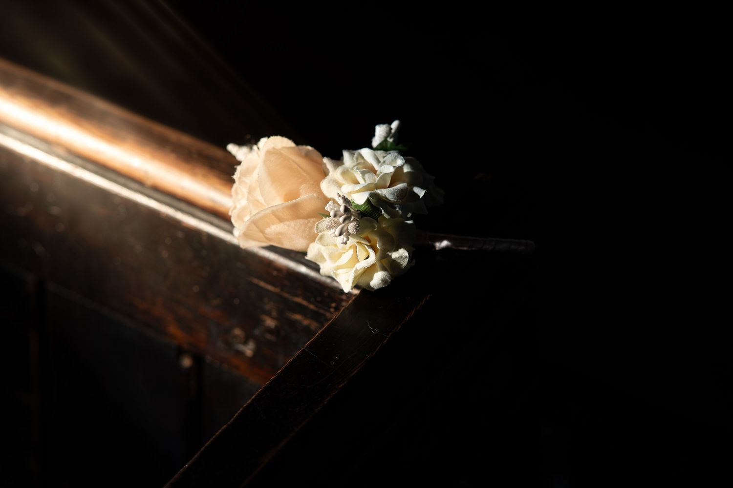 Artistic close-up of wedding rings and flowers in dramatic lighting.