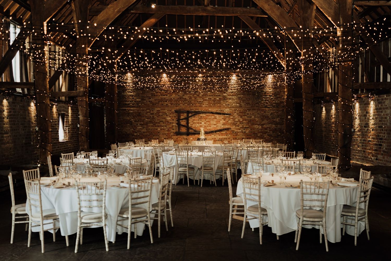 Reception venue with white tables and chairs under romantic string lighting.