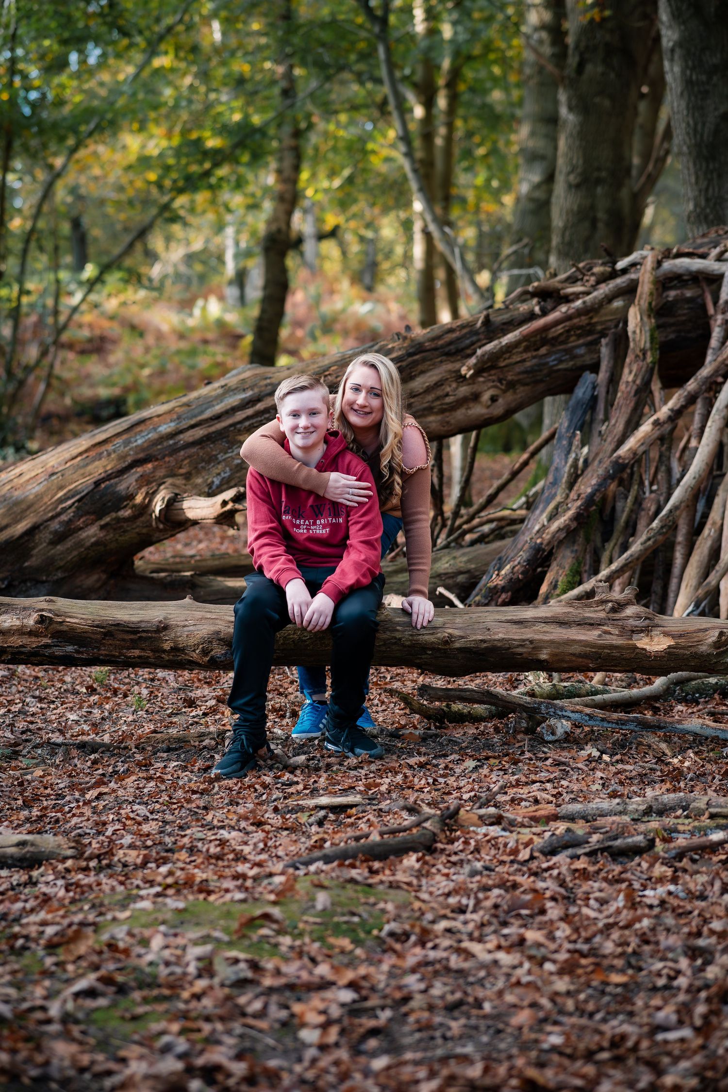 Two people sitting on fallen logs in an autumn forest setting.