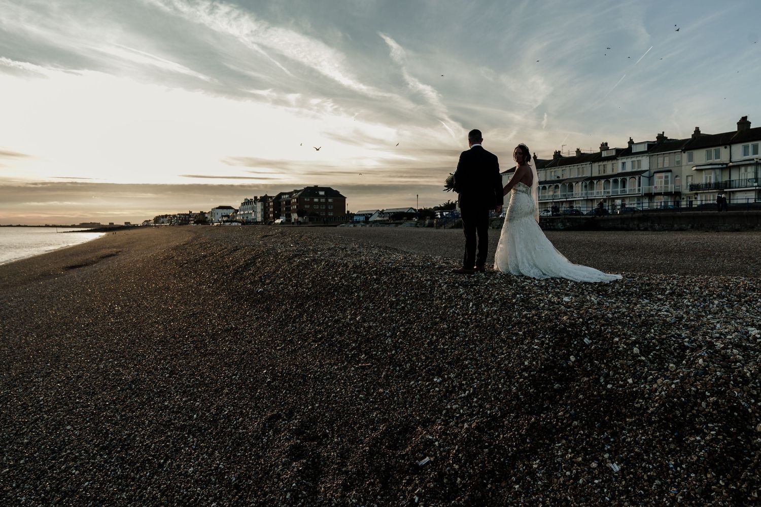 Dramatic coastal landscape with silhouettes against a sunset sky on a pebble beach.
