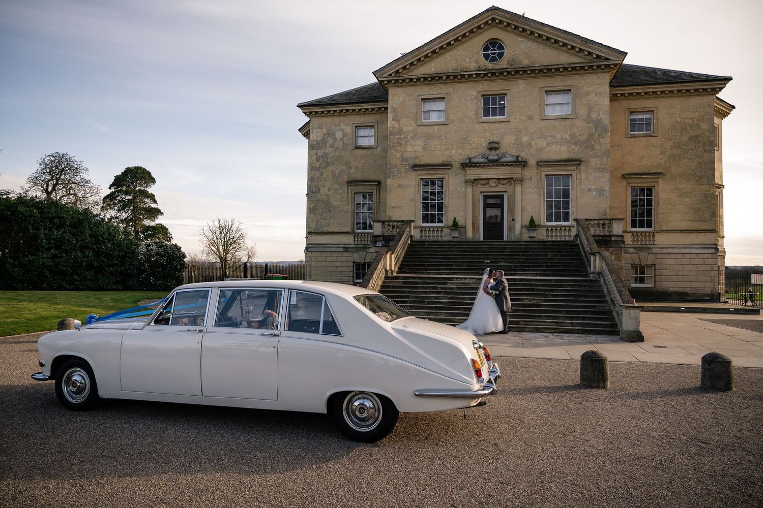 Elegant vintage white cars parked outside a grand stone manor house.
