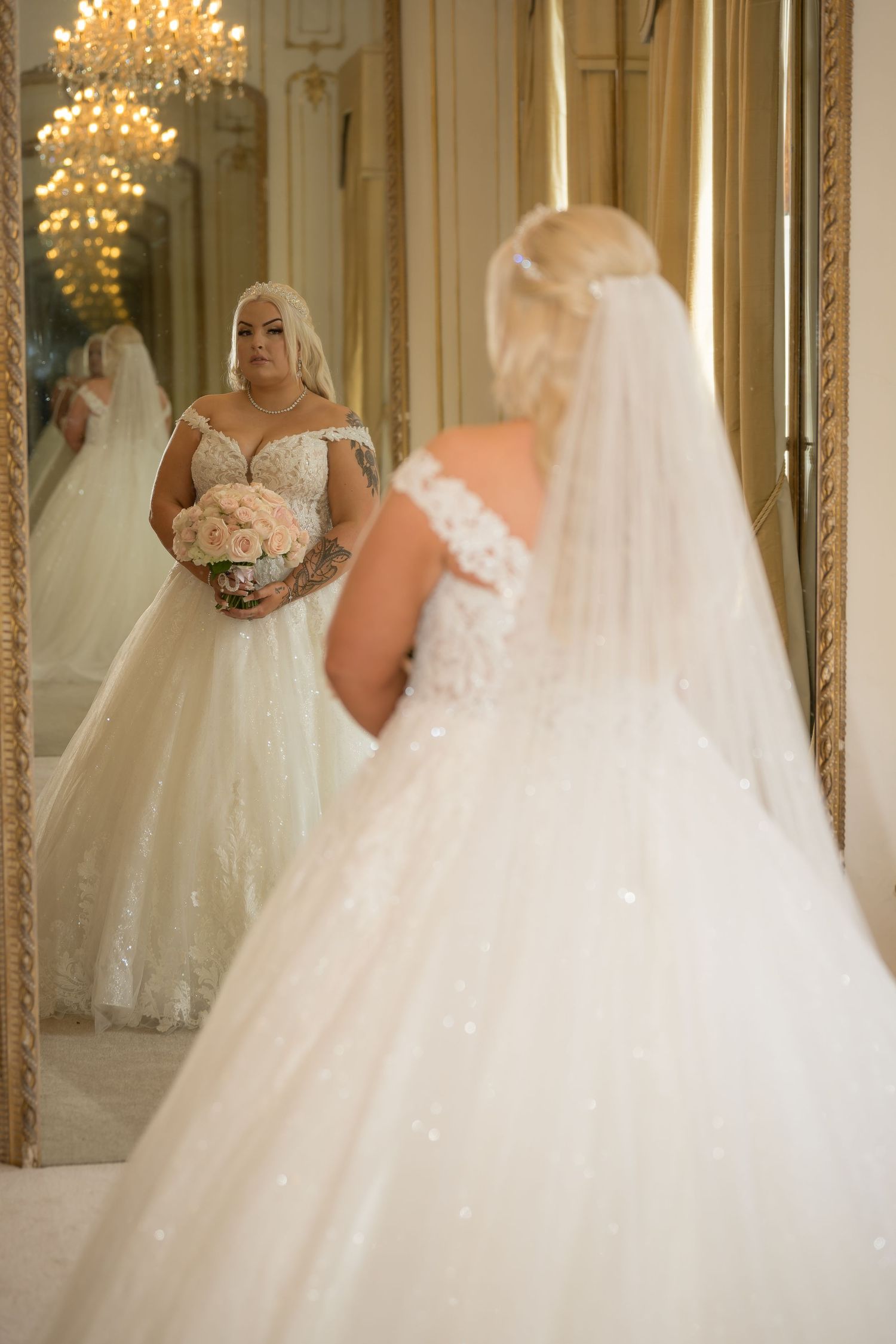 Elegant bridal gown reflections in ornate mirrors with crystal chandelier lighting.
