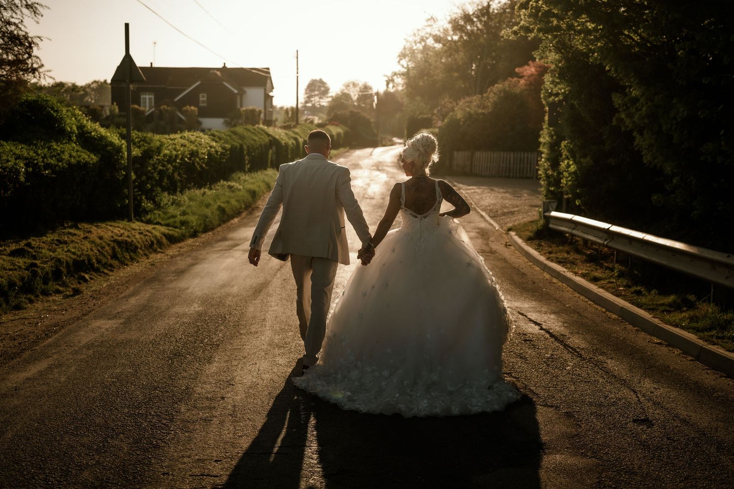 Silhouetted newlyweds walking down rural road during golden hour sunset.