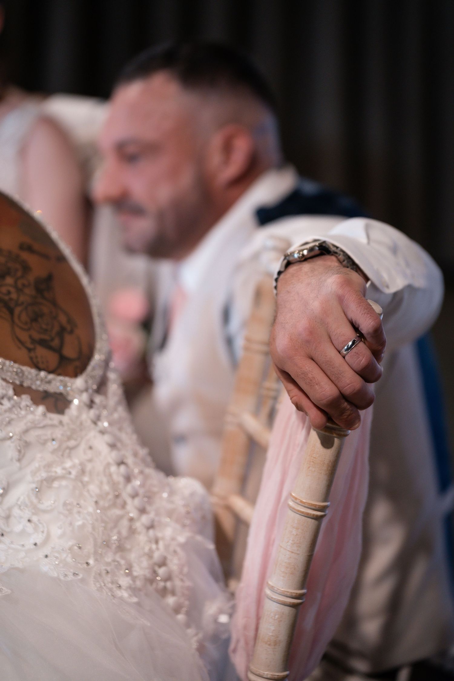 Close-up shot of wedding couple sitting on vintage chair showing ring and lace dress details.