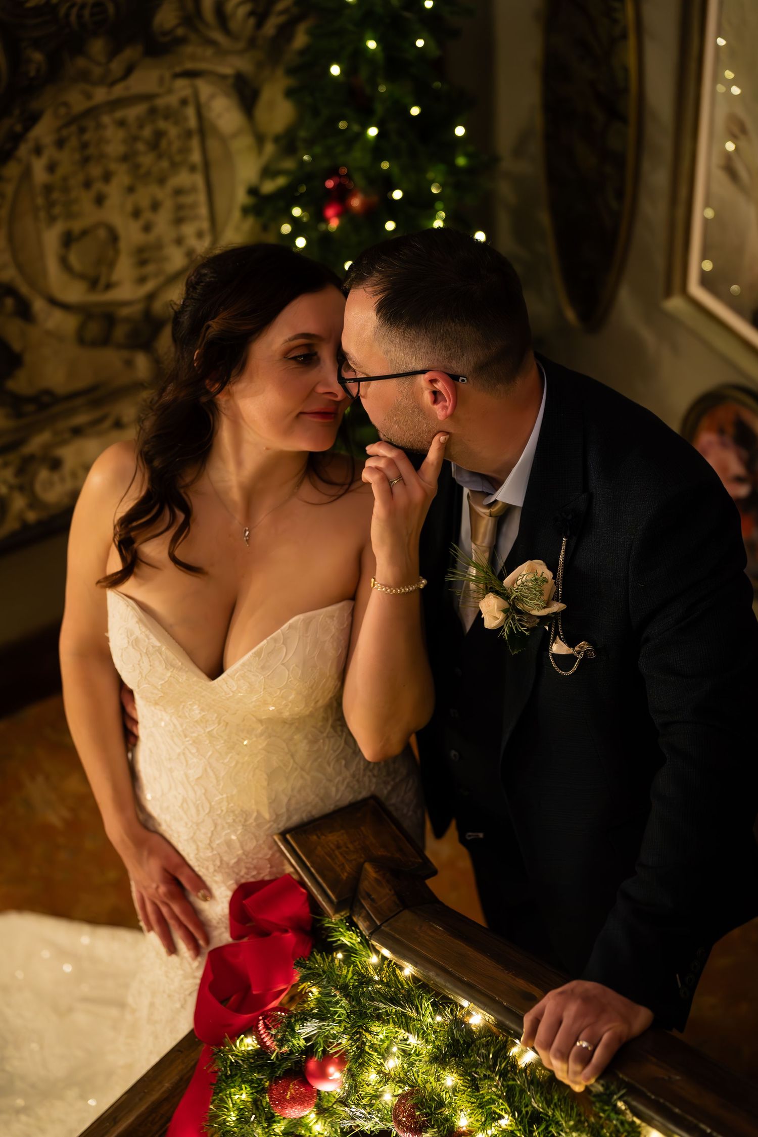 Couple shares intimate moment at reception table decorated with twinkling lights and red flowers.