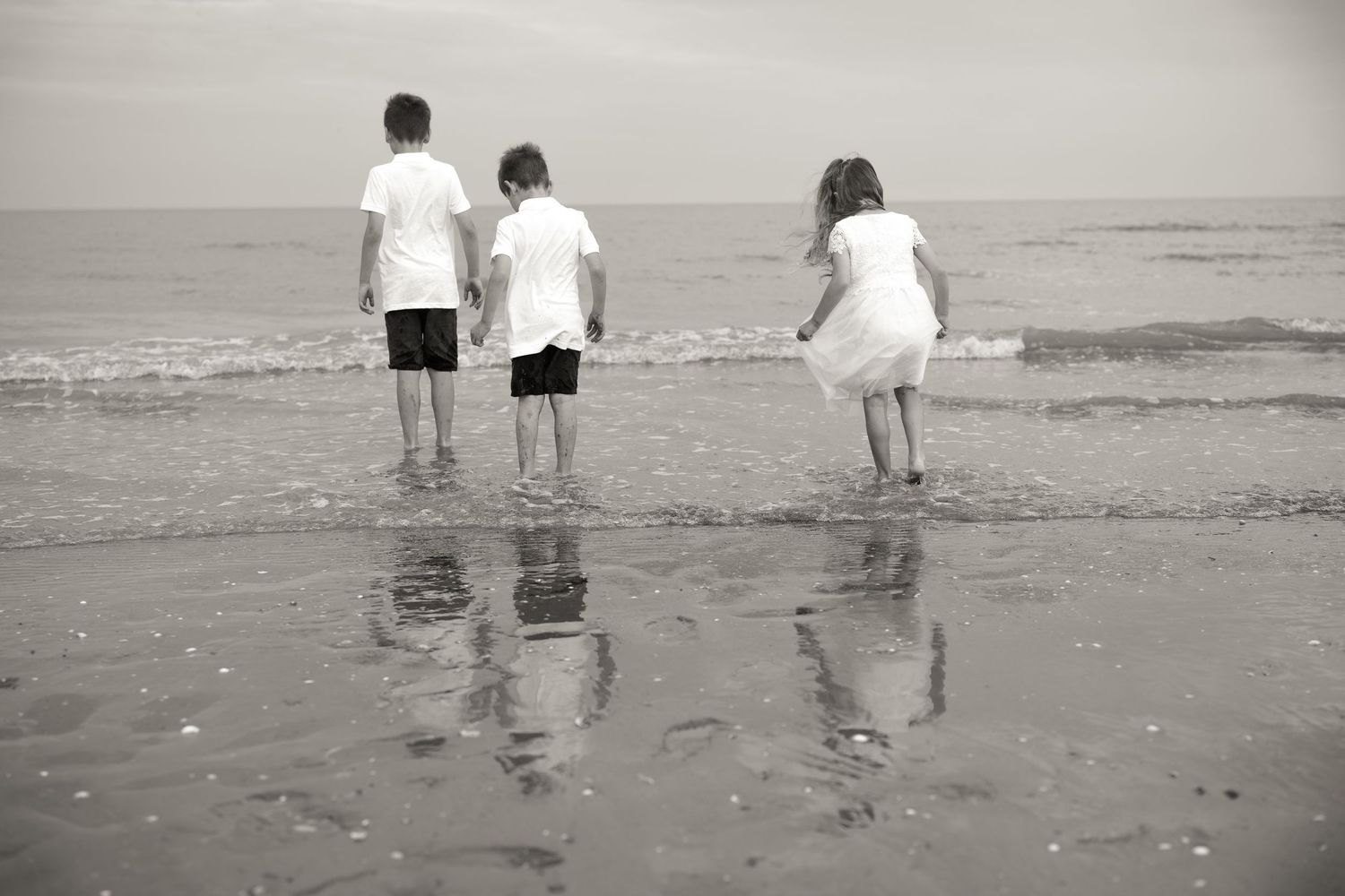 Black and white photo of children playing at the edge of the ocean.