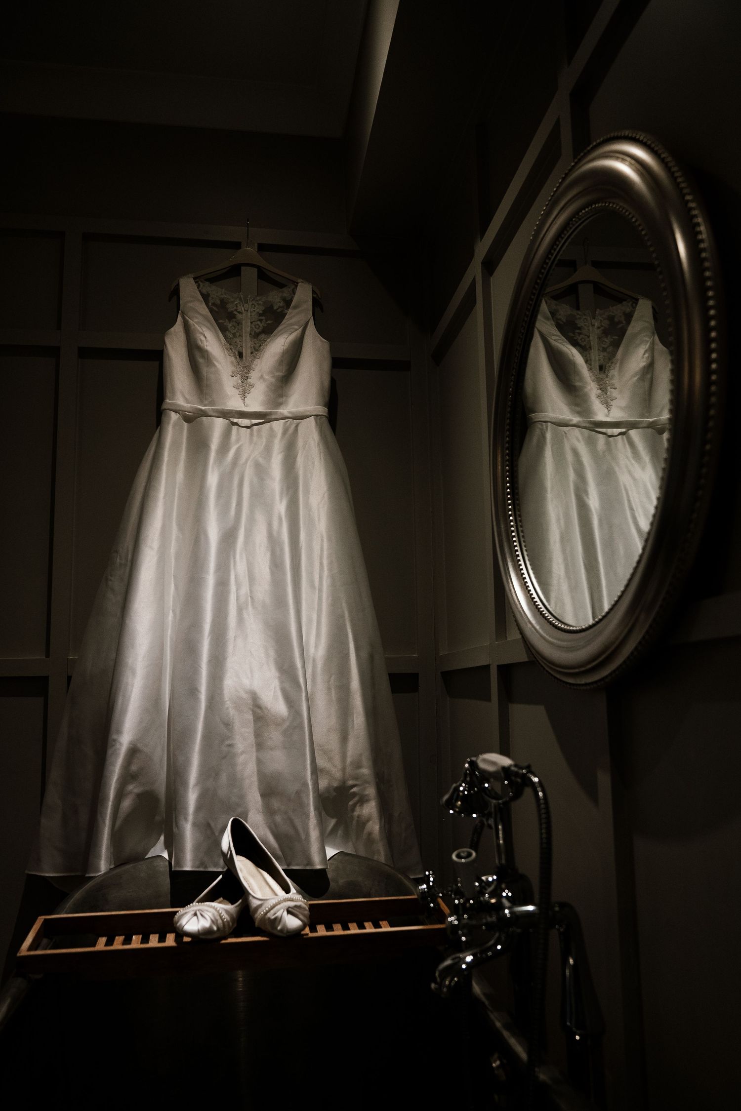 Wedding dress hangs elegantly in dramatic window light with shoes below.