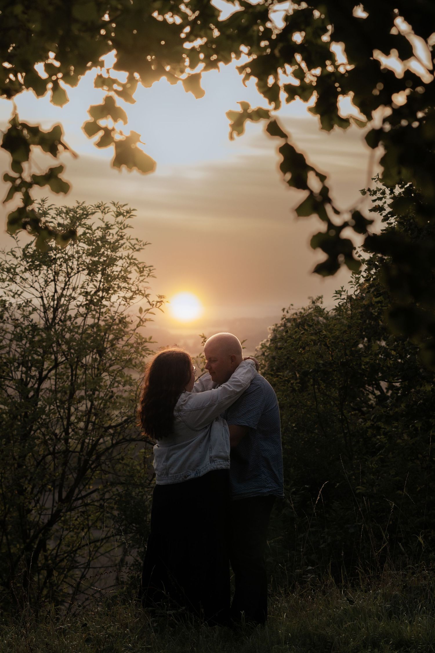 Romantic sunset photoshoot with couple silhouetted against golden sky and trees.