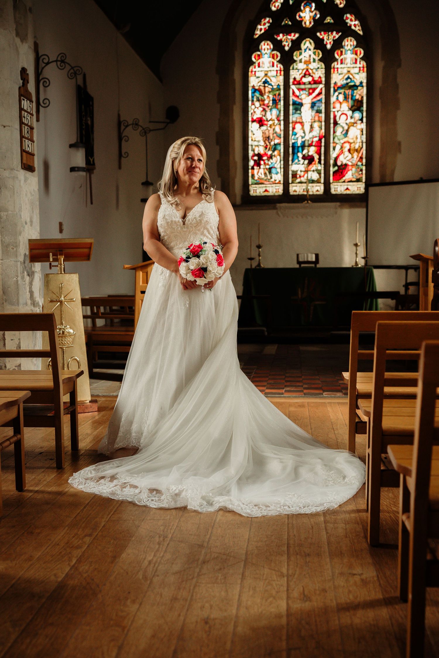 Elegant white wedding dress displayed in a historic church with stained glass windows.