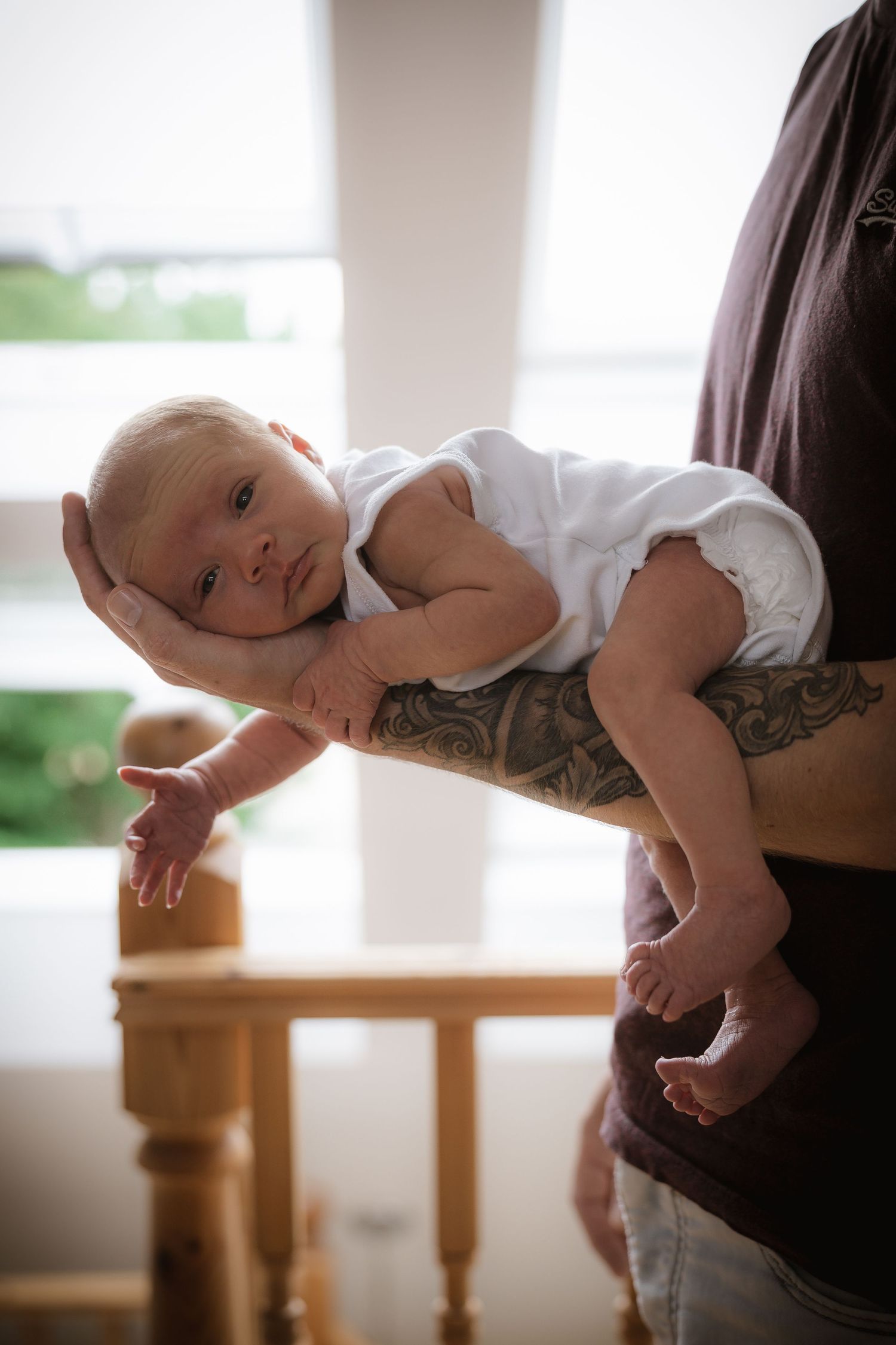 A sleeping baby rests peacefully against someone's shoulder in a bright room.