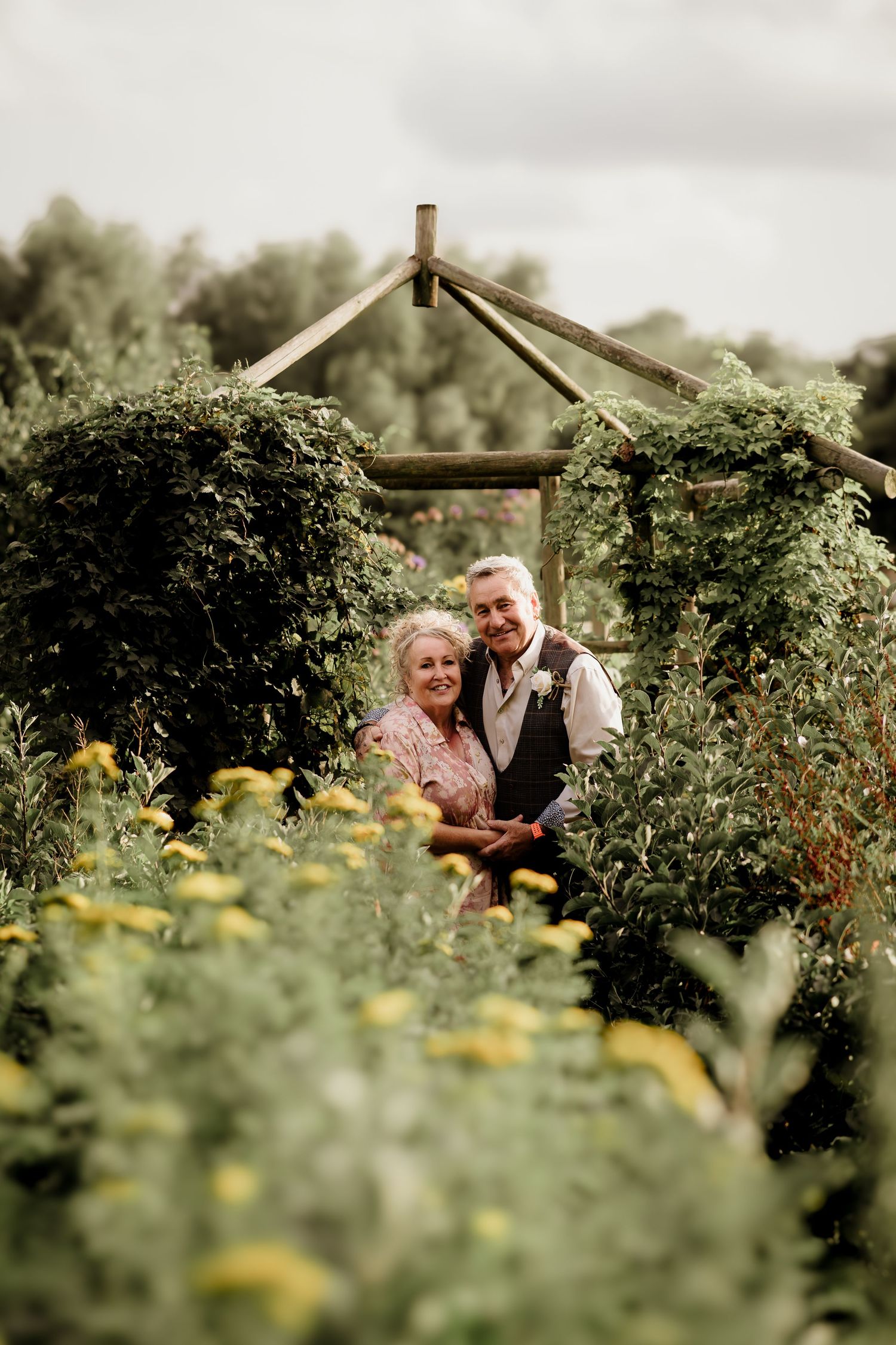 Romantic couple nestled among lush garden greenery and yellow flowers.