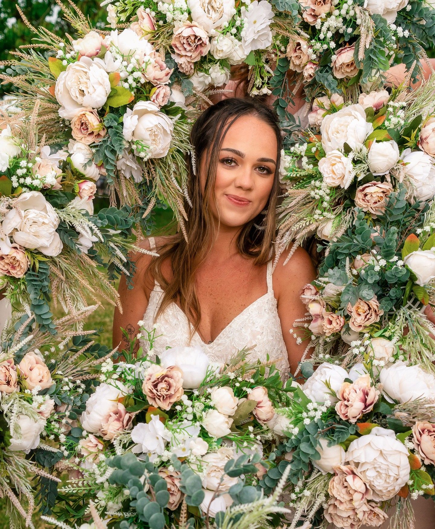 A stunning floral arch with pink and white roses frames a romantic bridal portrait.