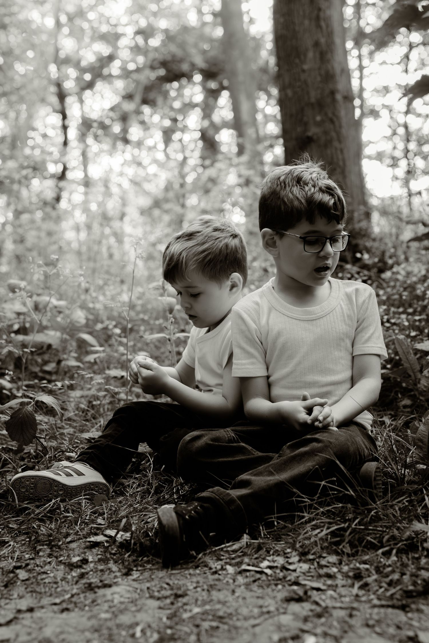 Black and white photo of children relaxing on forest ground surrounded by trees.