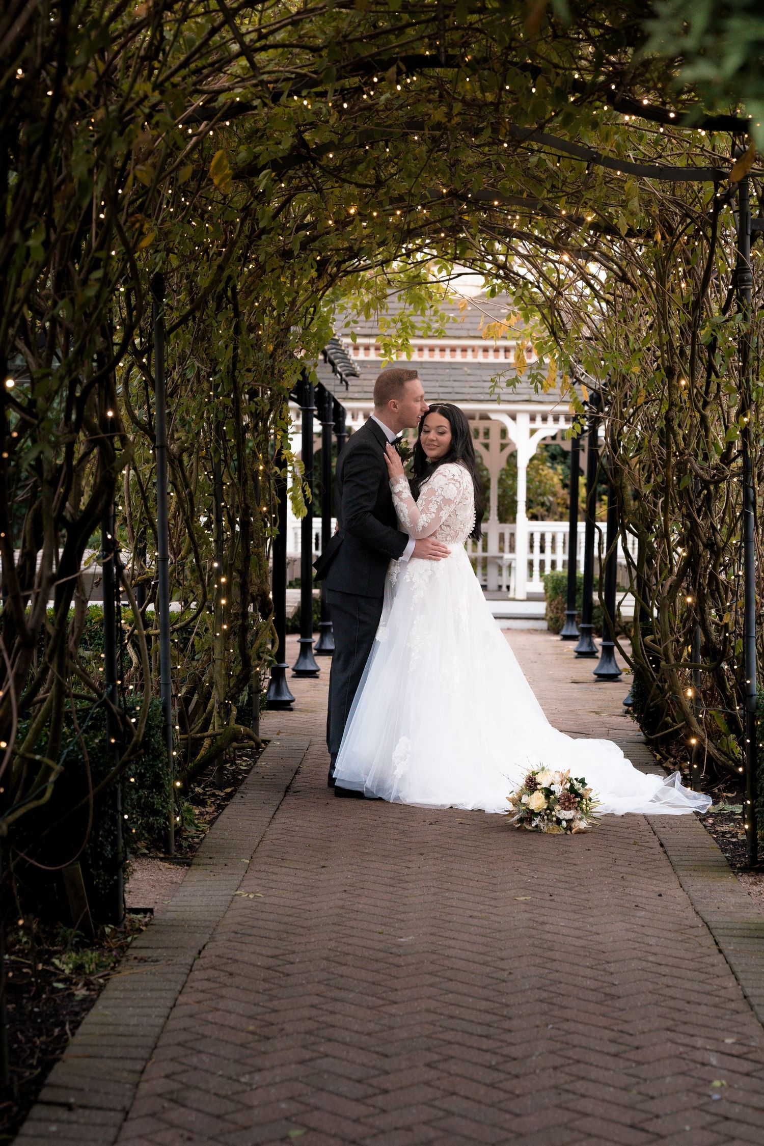 Wedding couple walks through enchanting garden tunnel covered in twisting vines and branches.