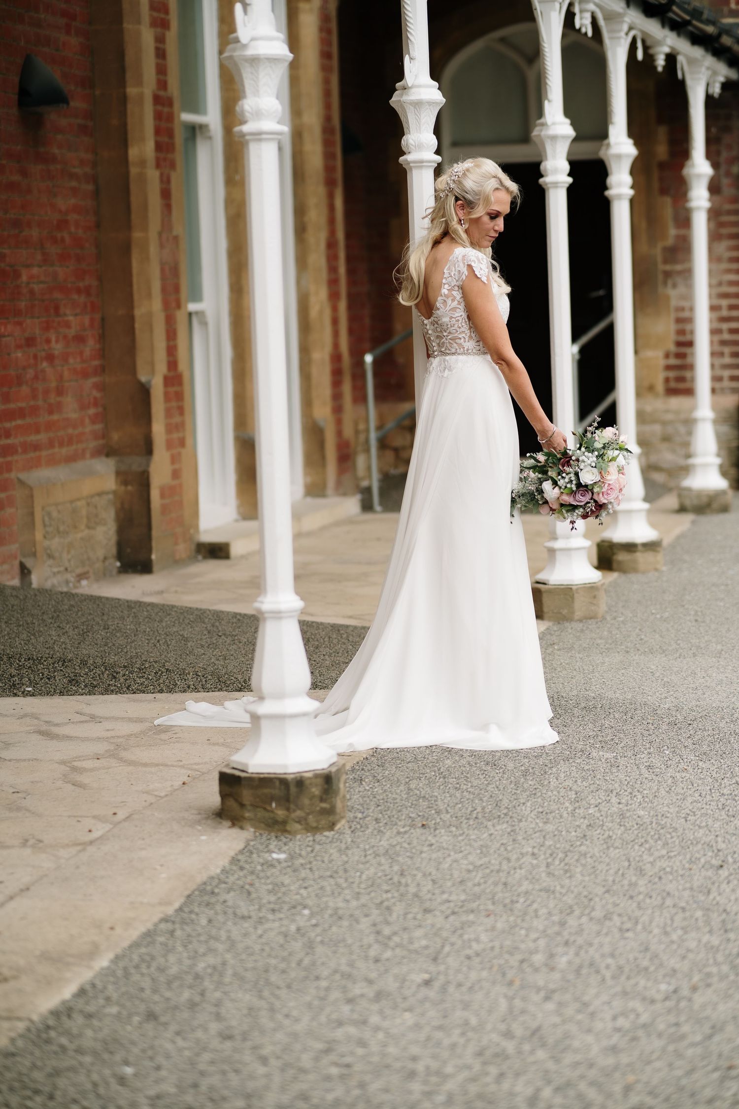White wedding dress flowing against brick building with classical white columns.