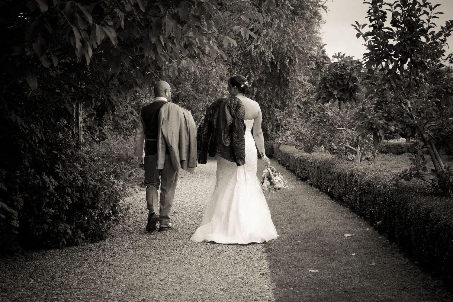 A couple walks down a tree-lined path in black and white wedding photography sequence.