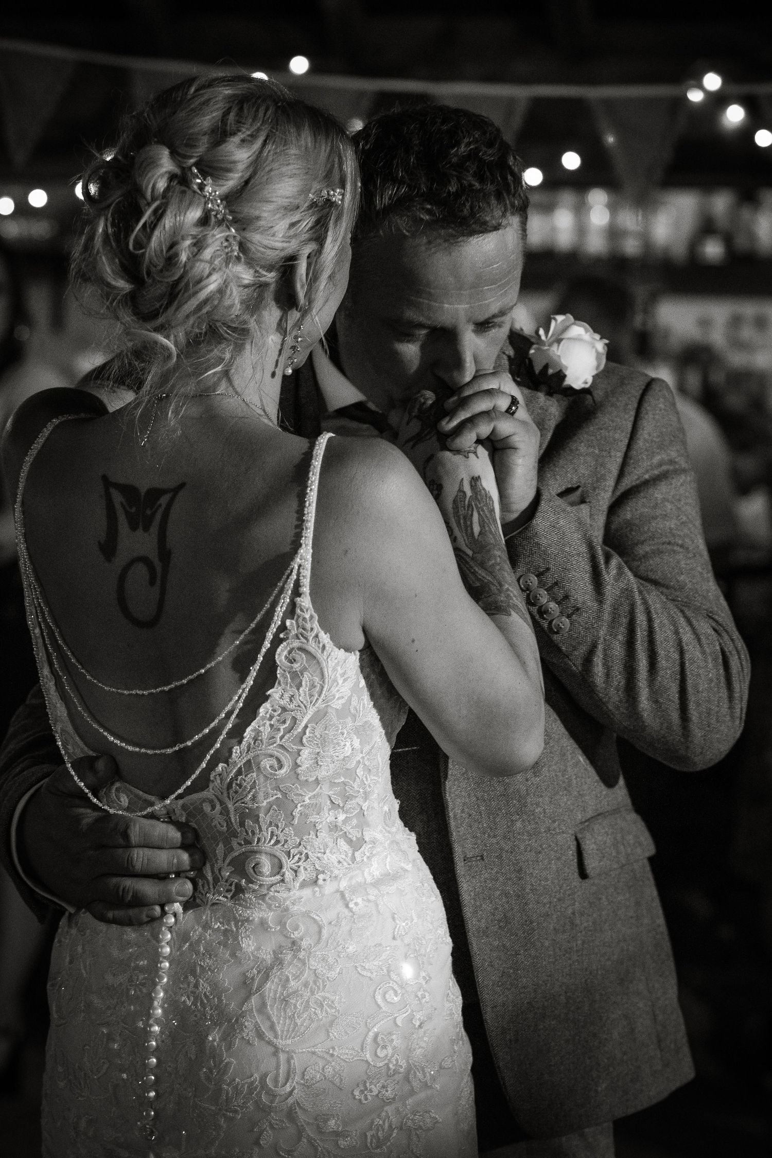 Black and white photo of a couple dancing under string lights at their wedding reception.