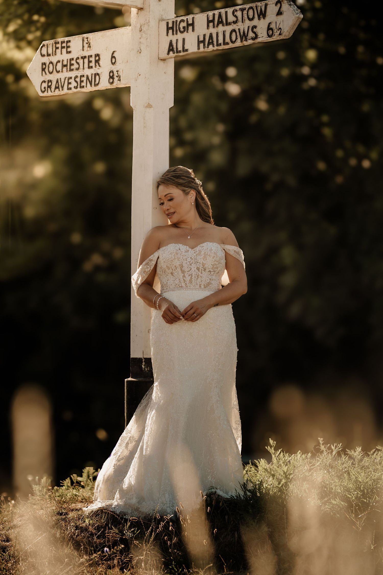 White wedding dress photographed against a rustic street sign in golden sunlight.