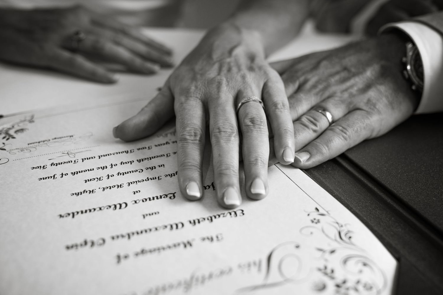 Close-up of hands signing wedding documents in black and white.