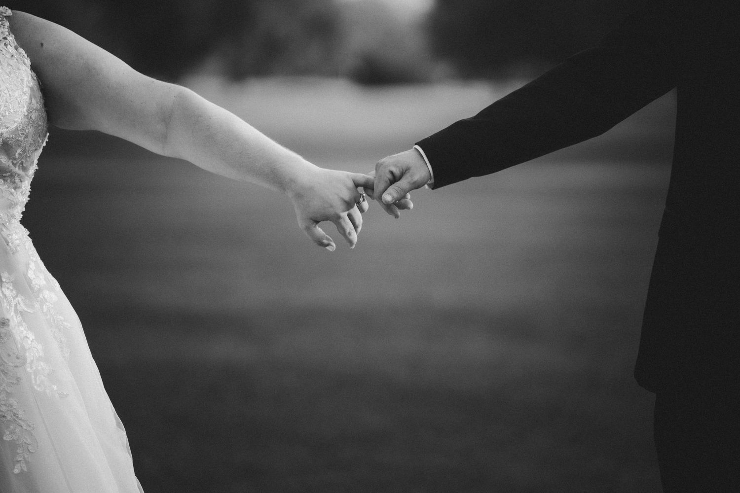 Black and white detail shot of hands in formal wedding attire.