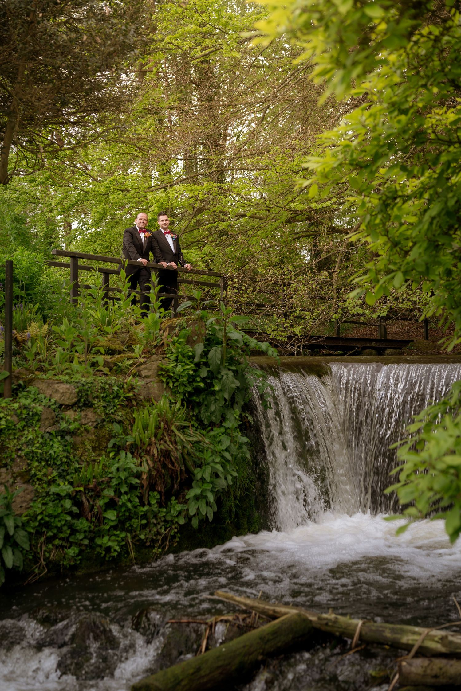 A scenic waterfall cascades beneath a wooden bridge surrounded by lush green foliage.