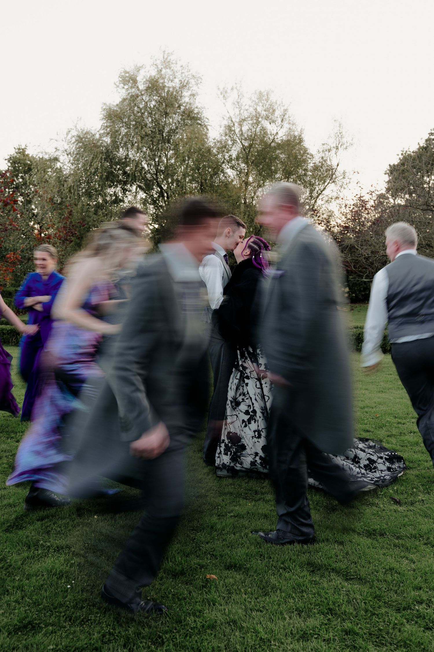 Motion blur photograph of wedding guests dancing on grass at outdoor reception.