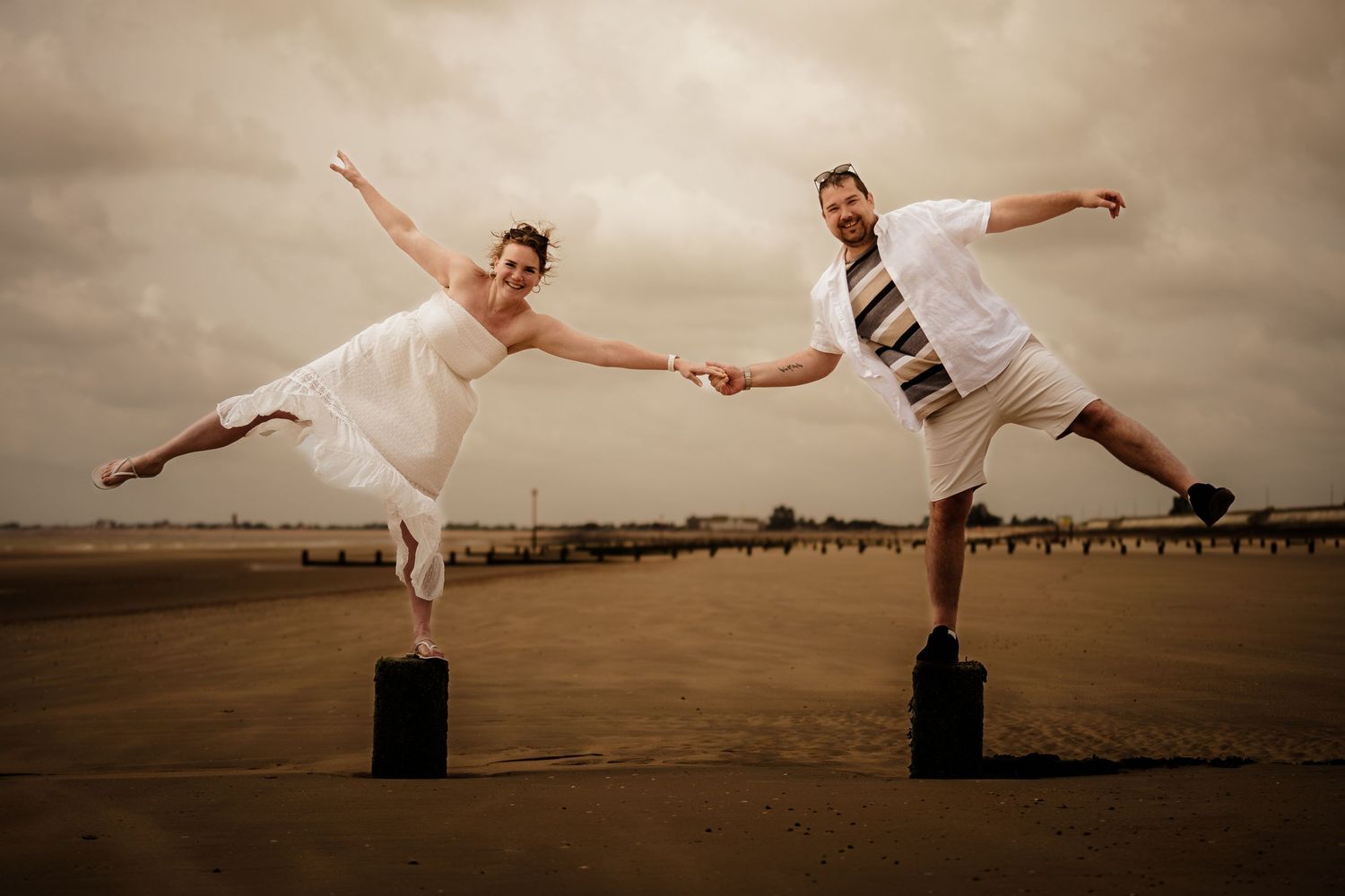 Artistic beach photoshoot showing playful poses with wooden posts at sunset.