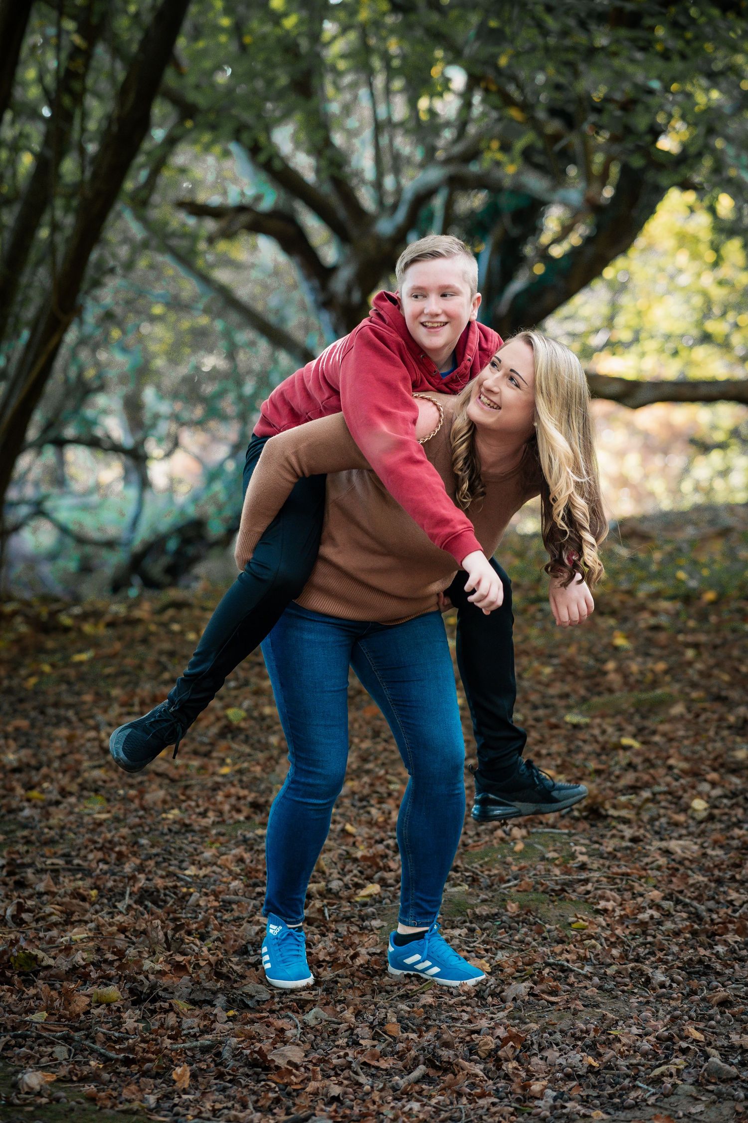 Playful couple laughing together on autumn forest ground covered in fallen leaves.