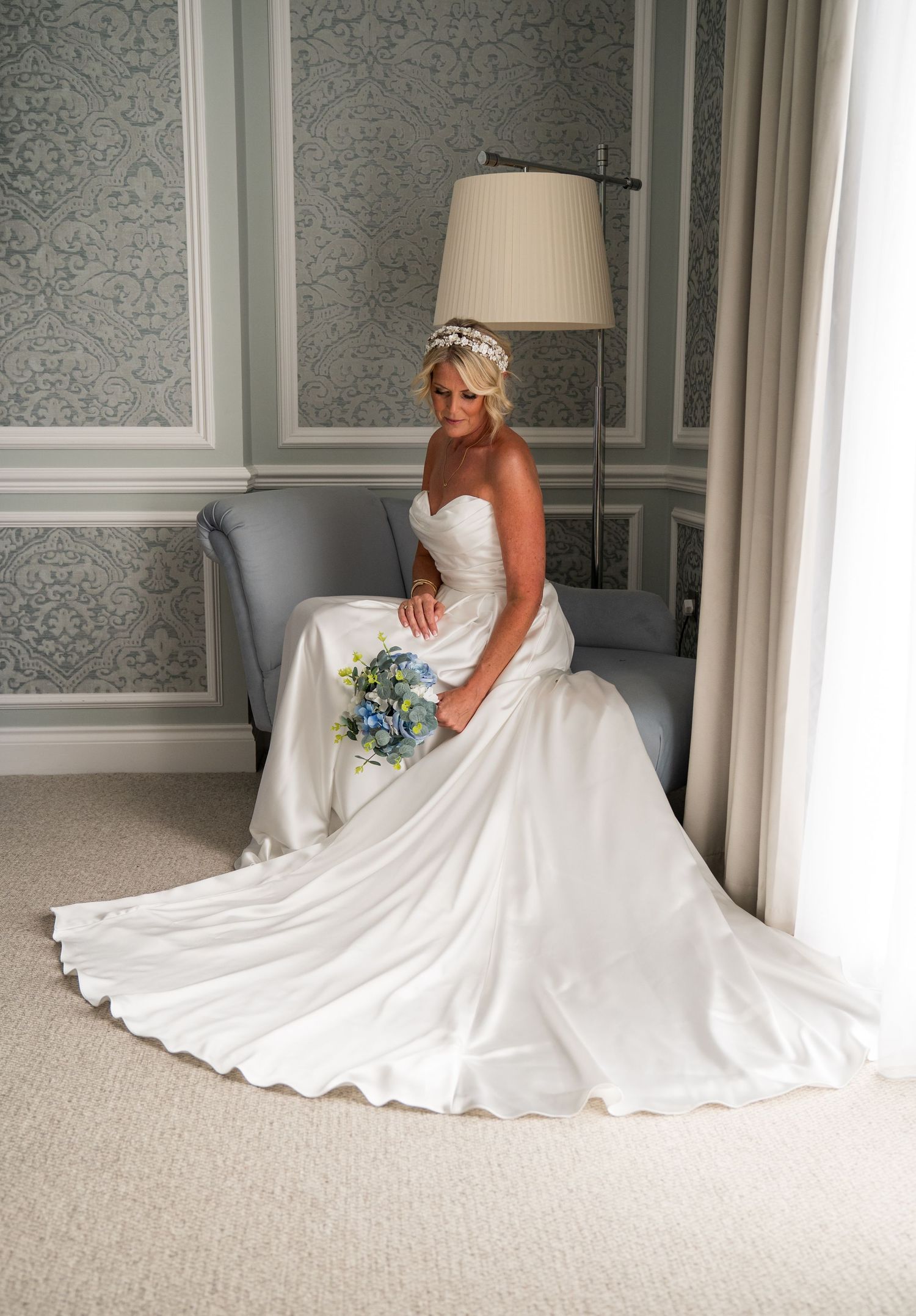 Bride in flowing white wedding gown sitting gracefully in an elegant grey room.