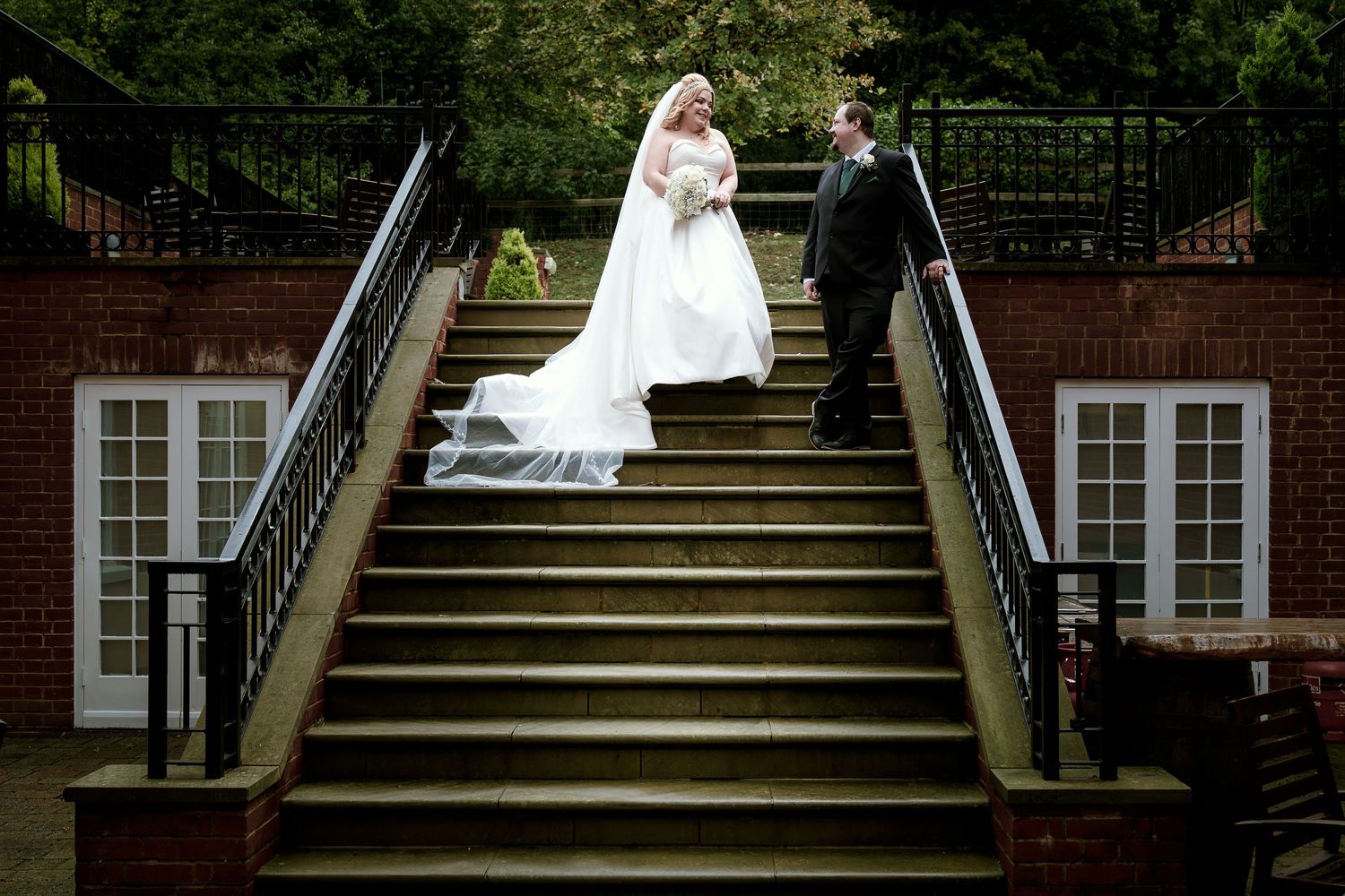 Wedding party arranged on grand outdoor staircase of historic brick building.