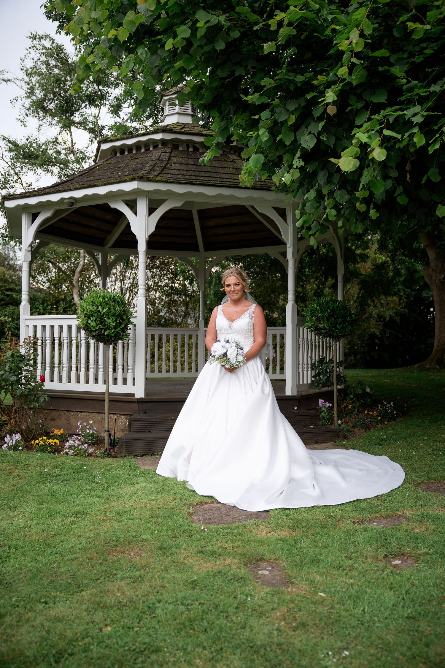 White gazebo in lush garden setting with floral arrangements.