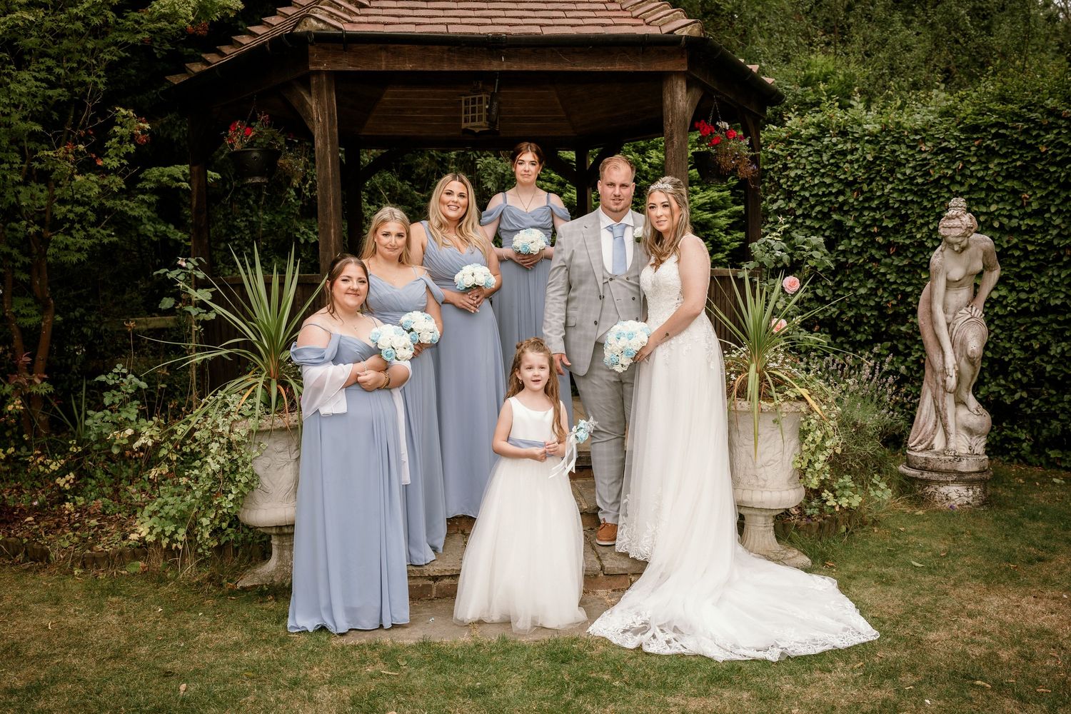 Wedding party poses in a garden setting with bridesmaids in light blue dresses.
