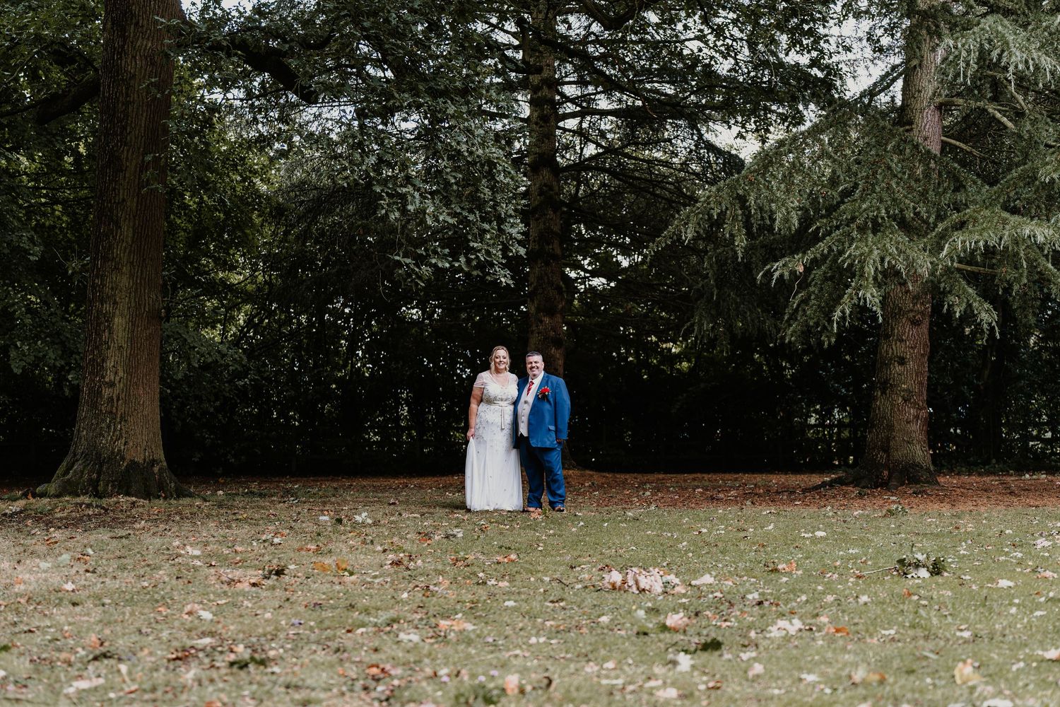 Wedding couple walking through a serene wooded area with tall trees.