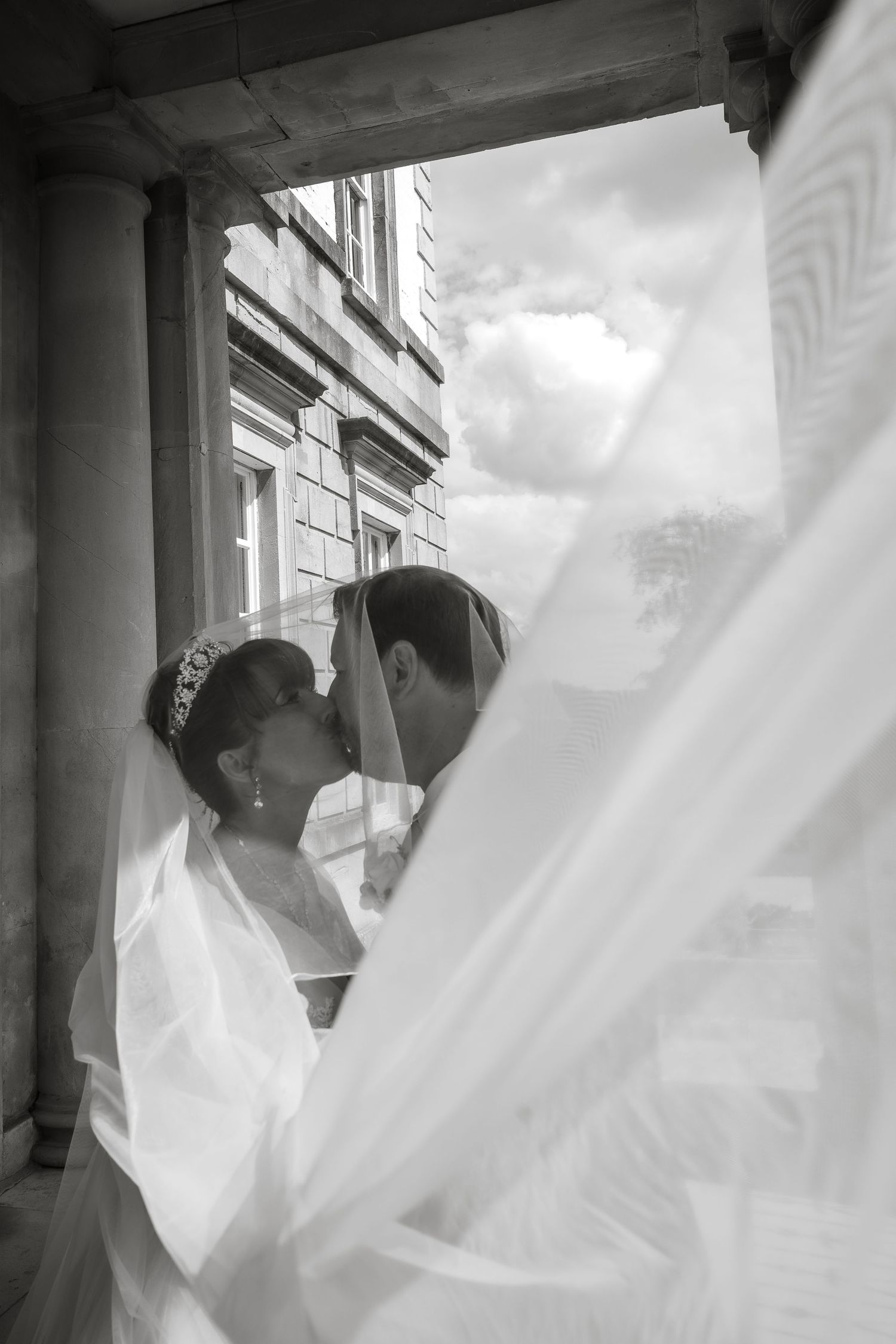 Flowing white wedding dress veil caught in a dramatic breeze against classic stone architecture.
