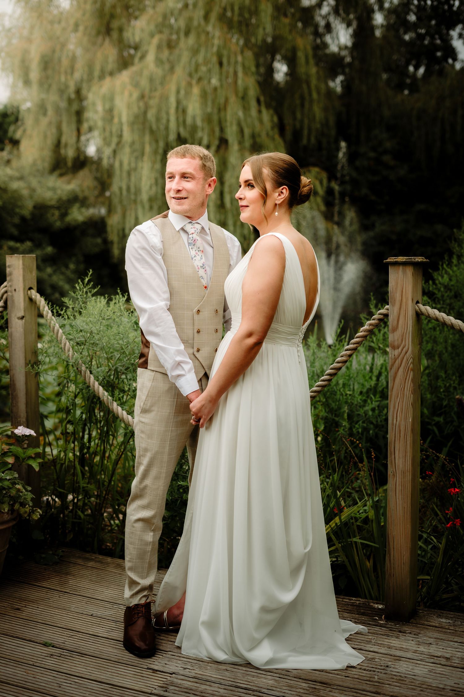 Wedding couple standing together on a wooden boardwalk surrounded by weeping willow trees.
