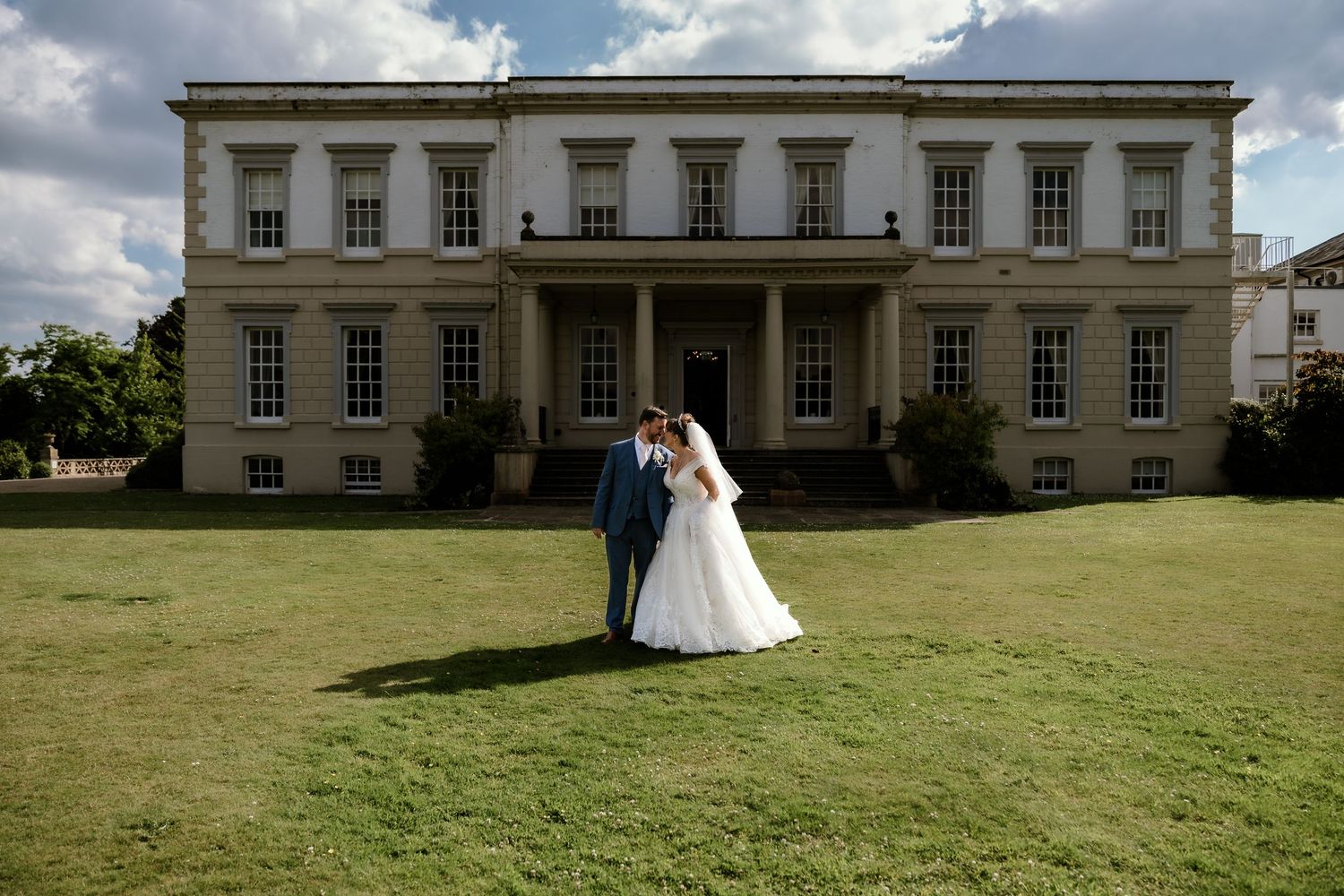Panoramic view of a stately manor house with expansive green lawn.