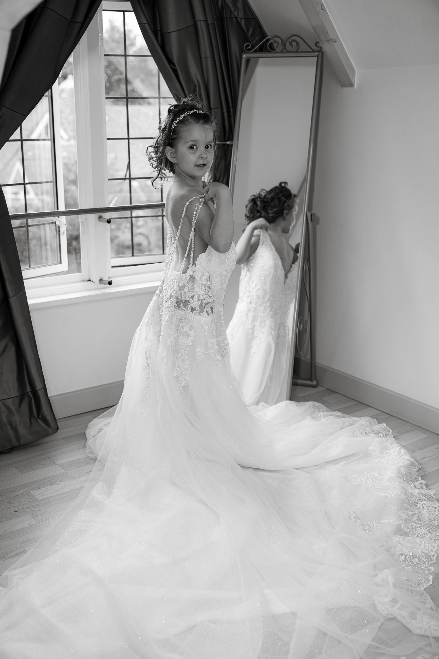 White wedding dress with intricate lace details and flowing train in a sunlit room.