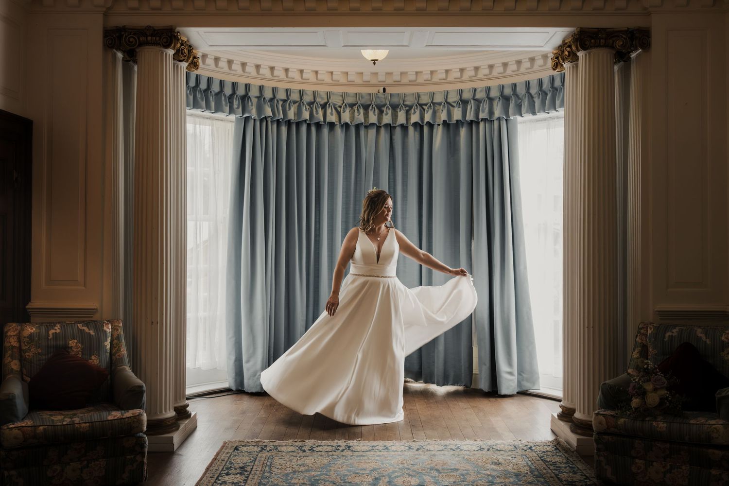 A panoramic view of a wedding dress flowing across a room with blue curtained windows.