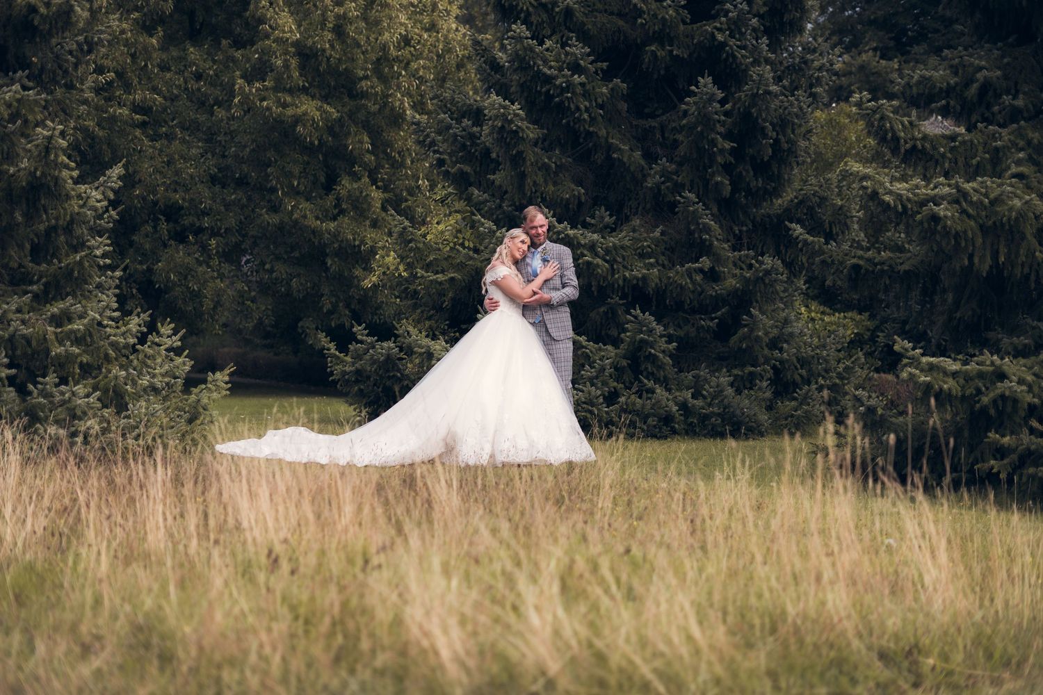 Wedding couple walking through tall grass in natural meadow setting.